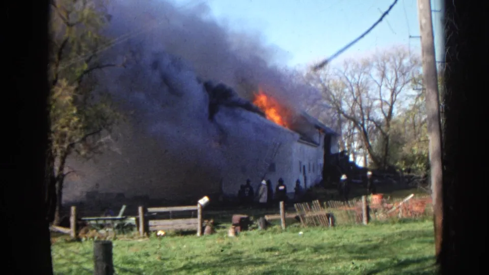 Wauconda, Illinois 1968 home-movie frame showing firefighters at a rural structure fire with heavy smoke overhead.