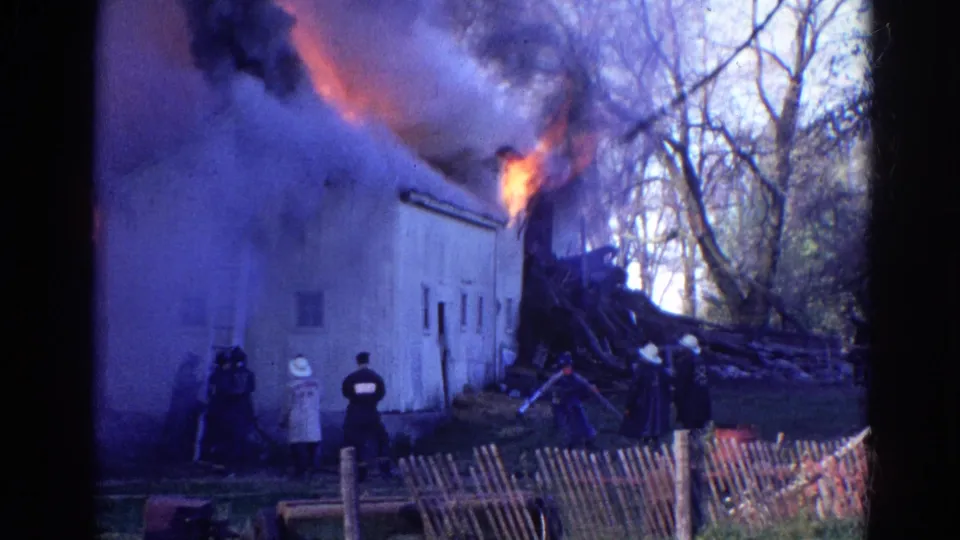 1968 Wauconda, Illinois home-movie frame with firefighters near a smoky building as flames burn along the roof area.
