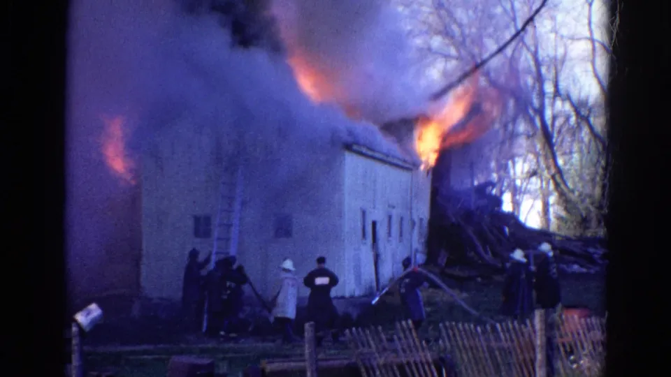 1968 Wauconda, Illinois 8mm frame showing a ladder against a burning building and firefighters working with hoses nearby.