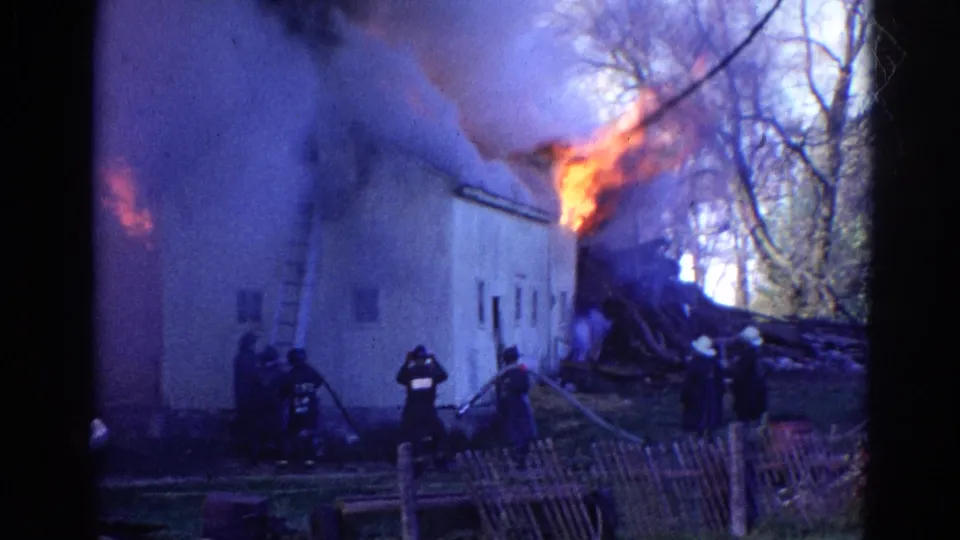 1968 Wauconda, Illinois 8mm frame showing firefighters with hoses near a light-colored building as flames and smoke rise above it.
