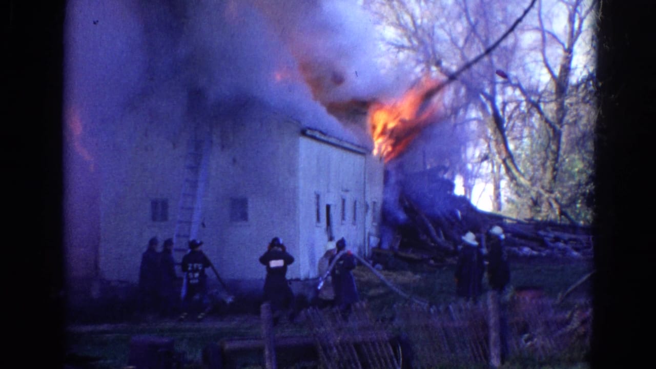 1968 Wauconda, Illinois 8mm frame showing firefighters near a white rural building as flames and dark smoke rise from the roofline.