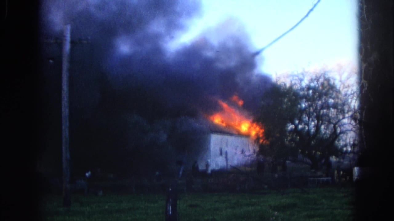 1968 Wauconda, Illinois home-movie frame showing a dense smoke plume above a white house, with orange fire visible near the roof edge.