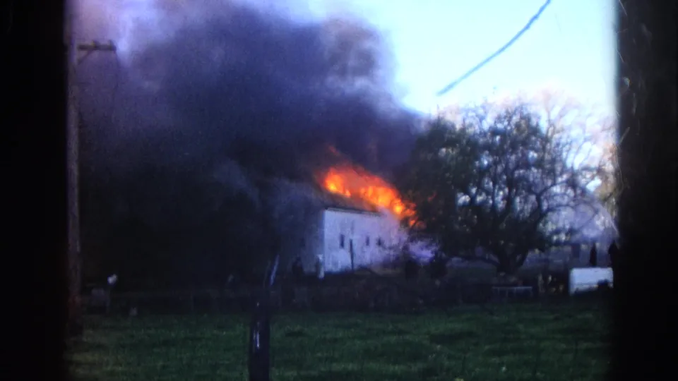 1968 Wauconda, Illinois 8mm frame of flames and black smoke coming from a white house, seen from across a grassy yard with trees nearby.