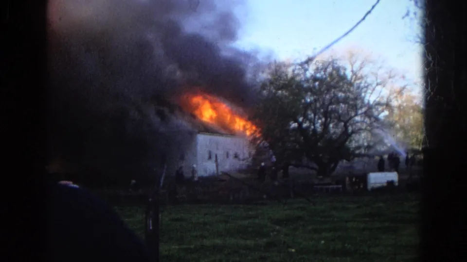 1968 Wauconda, Illinois frame with heavy smoke and flames along a white building's roofline, seen through dark 8mm frame edges.
