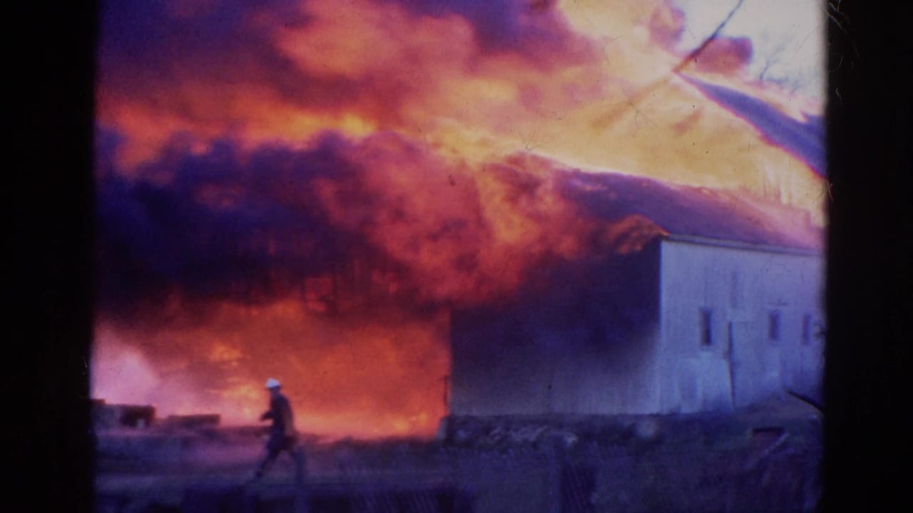 Firefighter standing near a burning rural building as thick smoke rises.
