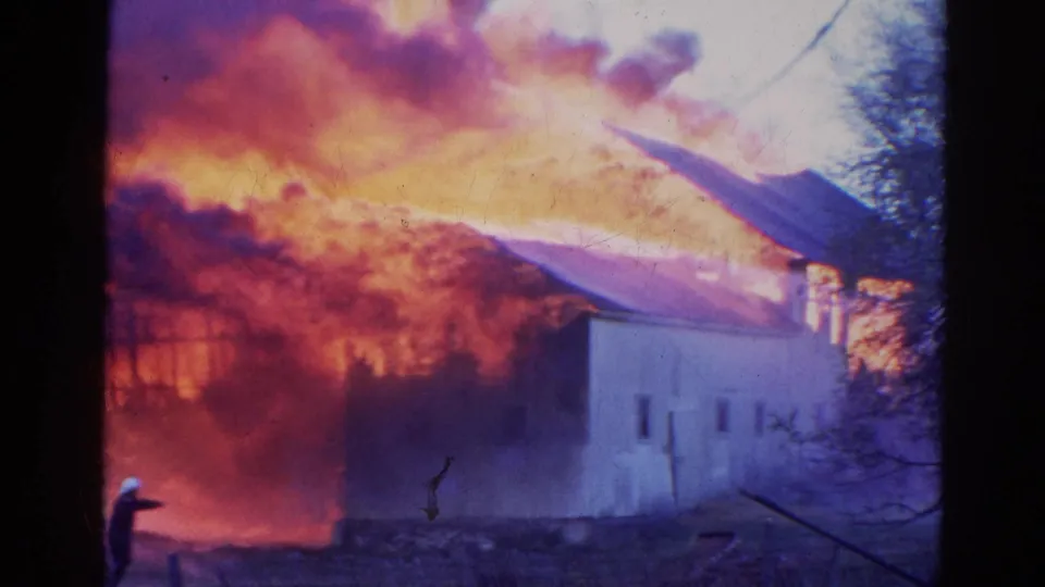 A firefighter in a white helmet appears near a burning structure in 1968 Wauconda footage, with smoke filling the sky.