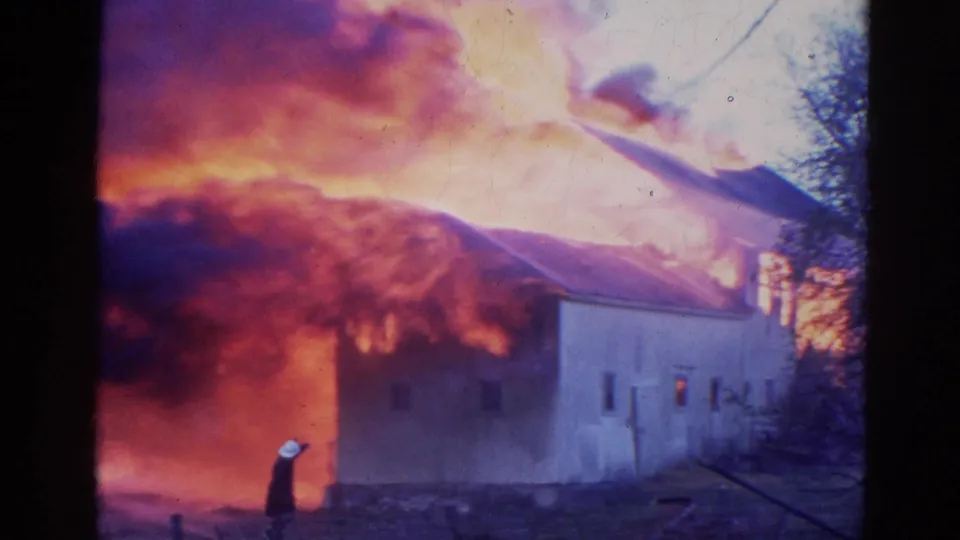 In this Wauconda fire scene, flames and smoke tower behind a pale building as a firefighter remains near the foreground.