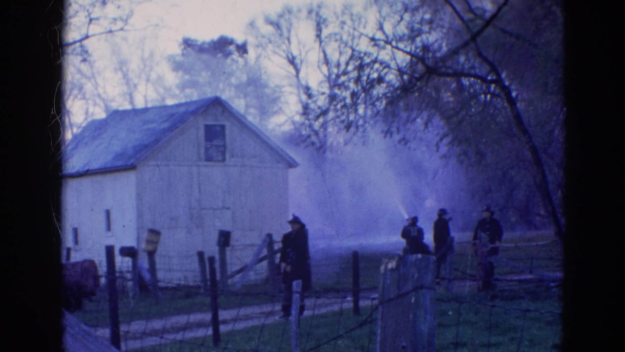 1968 Wauconda, Illinois 8mm frame showing firefighters spraying water toward a white barn from behind a rural fence.