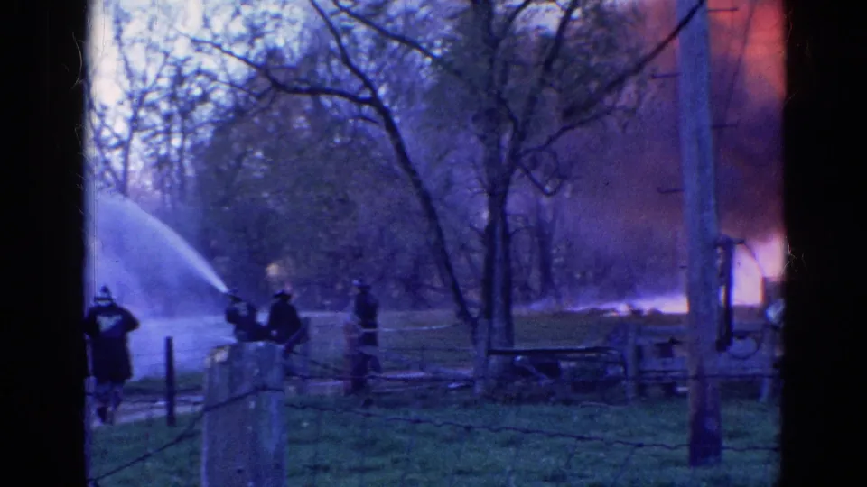 1968 Wauconda, Illinois 8mm frame showing firefighters spraying water near visible flames at the edge of a barn or structure.
