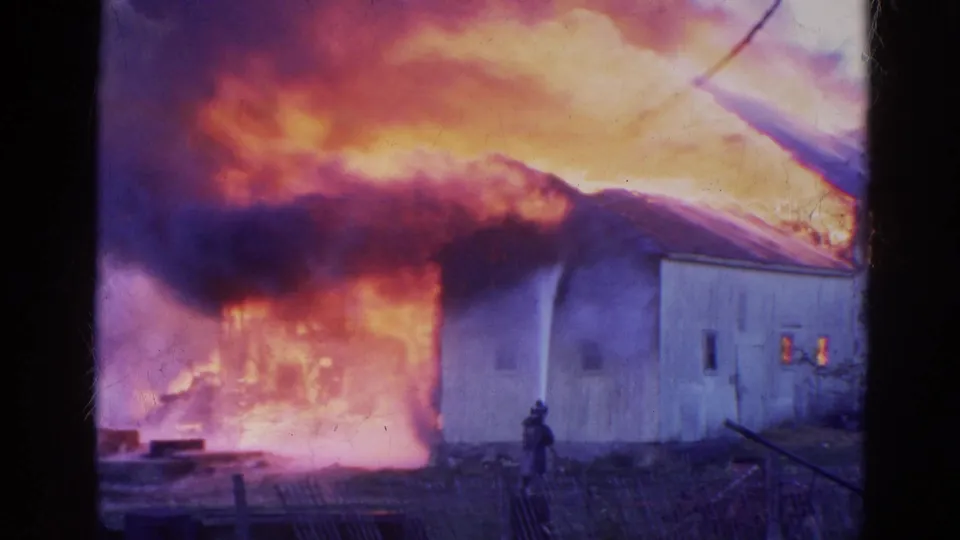 A firefighter sprays water at a heavily burning barn in metadata-identified 1968 Wauconda, Illinois home-movie footage.
