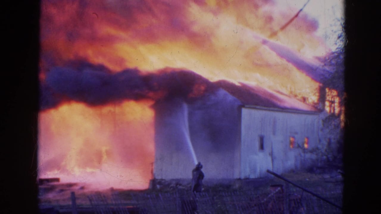 Firefighters spray water at a burning rural building as black smoke rises.
