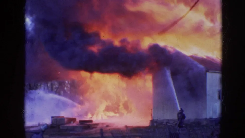 Firefighters battle a large Wauconda structure fire, with water spray crossing thick smoke and flames near the building wall.