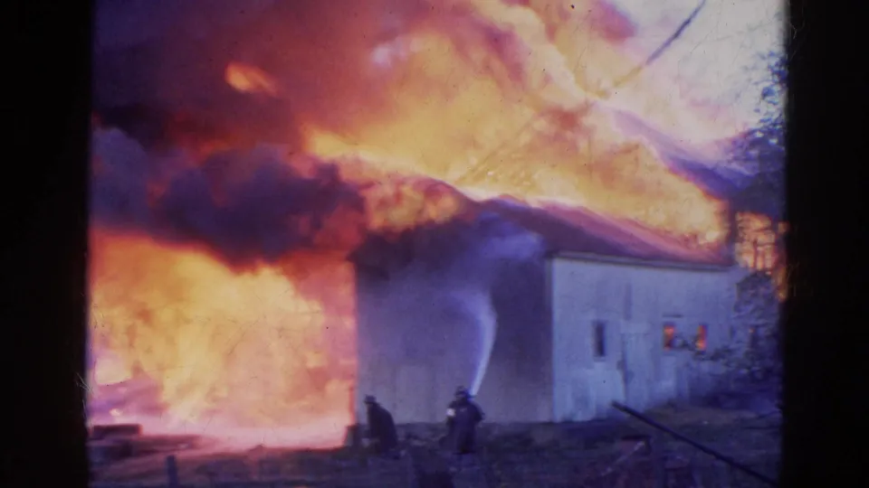 Firefighters direct water toward a burning structure in 1968 Wauconda, Illinois, with flames filling the background.