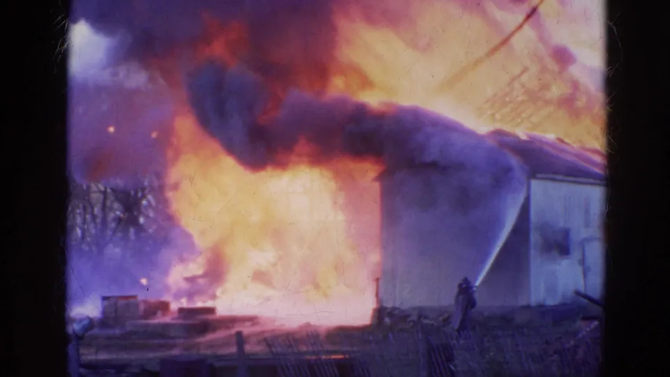 A firefighter directs a hose at a burning building in Wauconda, Illinois, with intense flames and smoke visible on 8mm film.