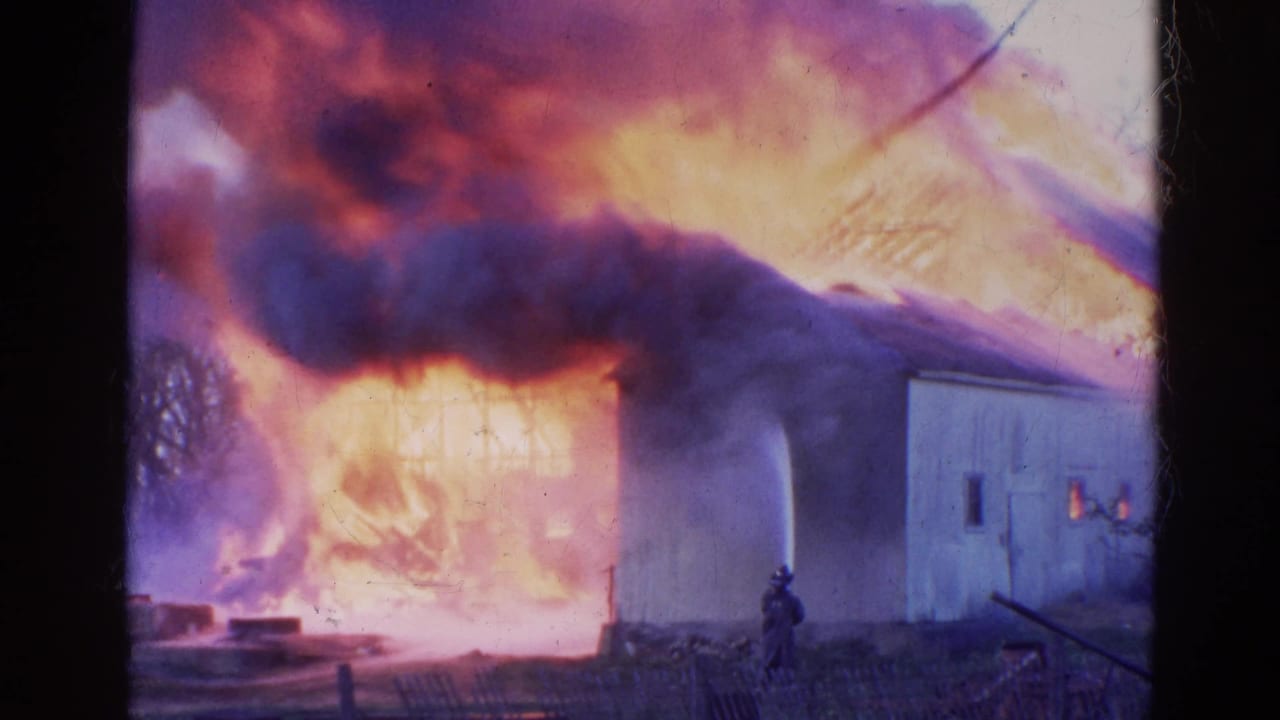 Flames spread across a building while smoke rolls above and a firefighter remains near the structure.