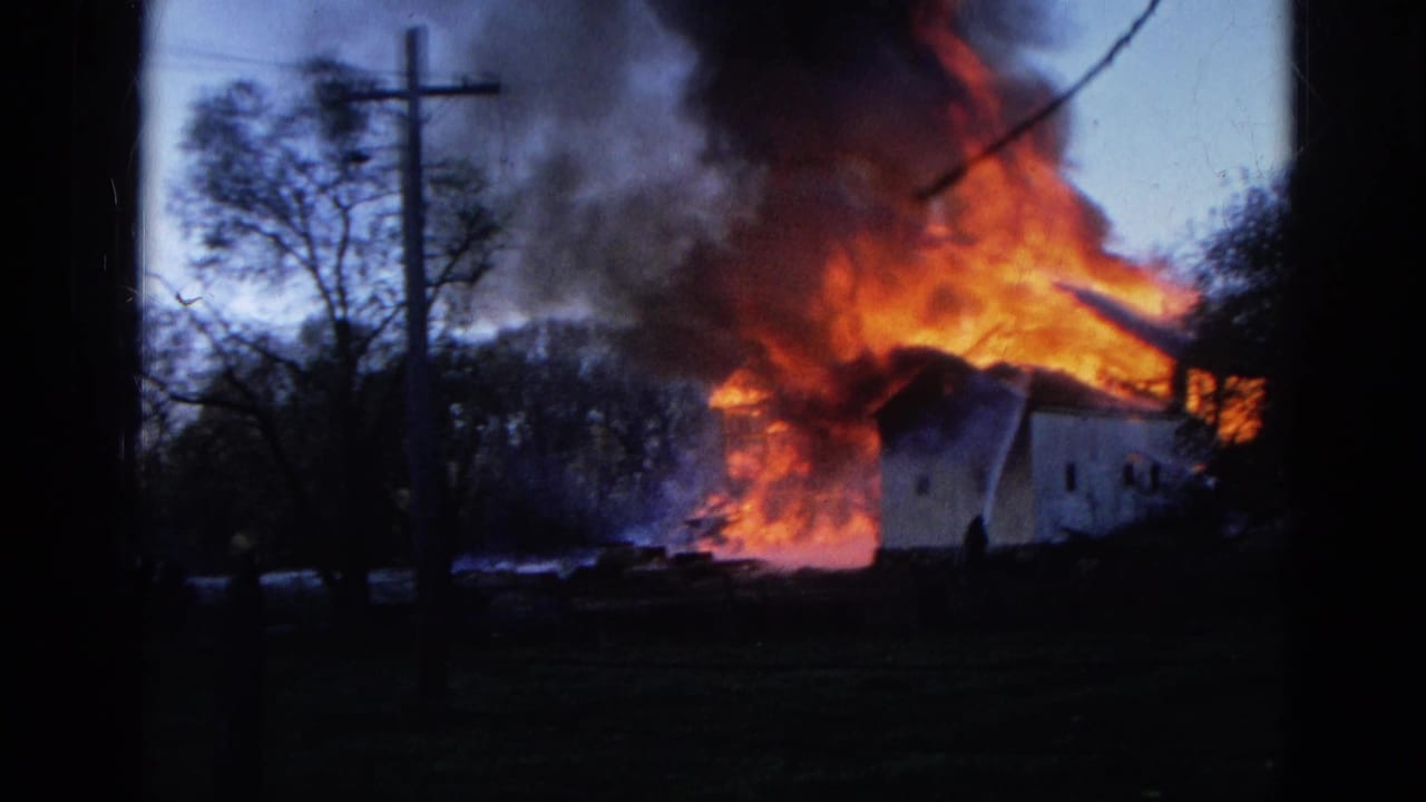 1968 Wauconda, Illinois 8mm frame showing a house or outbuilding on fire behind a utility pole, with dark smoke and bright roofline flames.