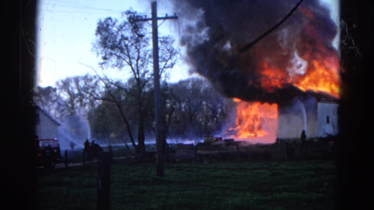 1968 Wauconda, Illinois 8mm frame showing a white house engulfed in flames, black smoke overhead, and water streams aimed at the fire.