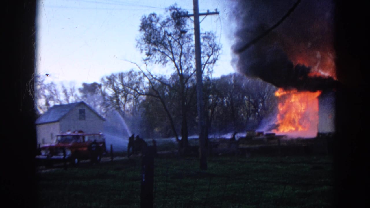 Red fire truck near a white house as flames and smoke rise from the right side.
