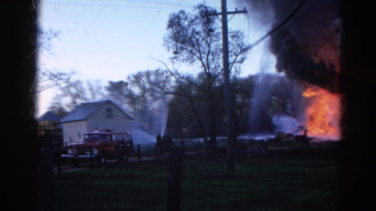 1968 Wauconda, Illinois 8mm frame showing water streams crossing a smoky yard toward flames at the side of a white house.