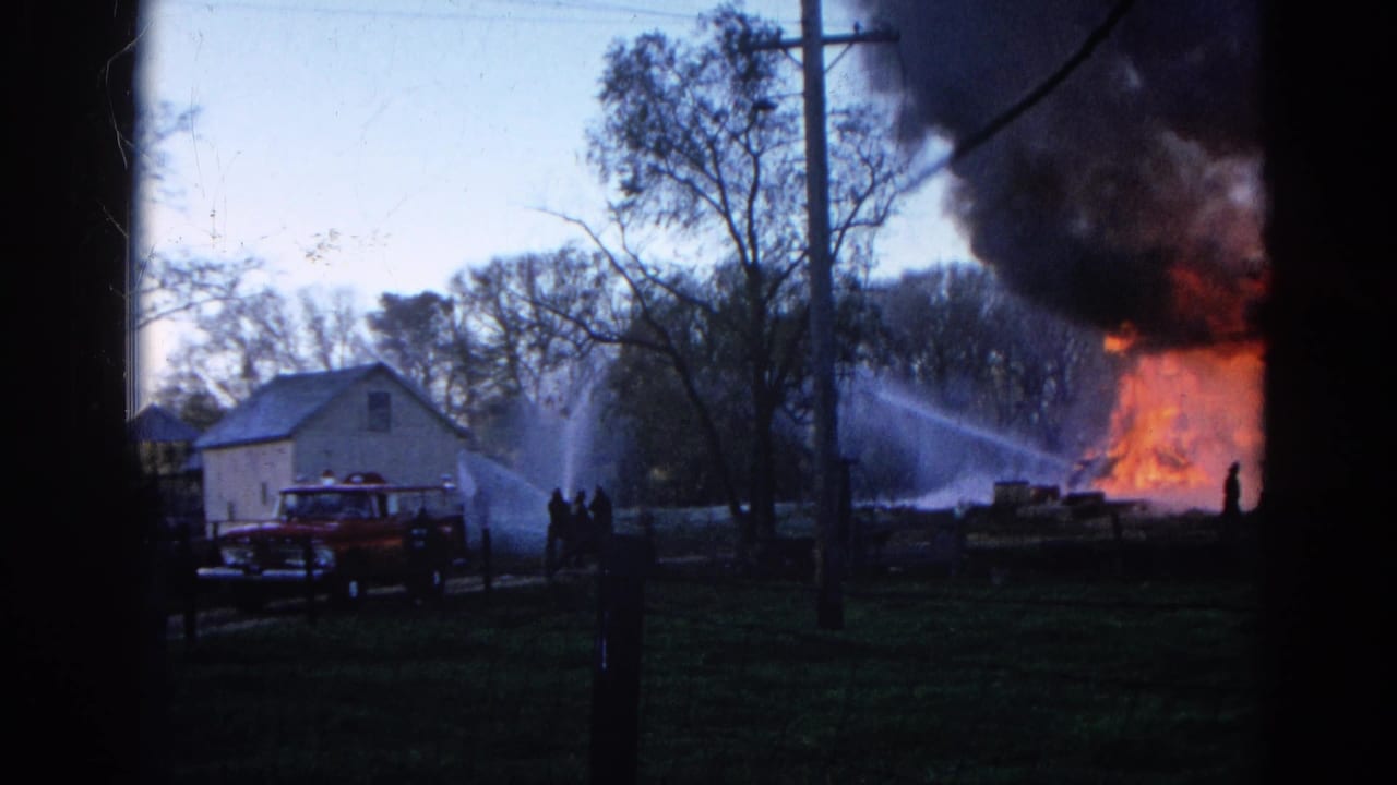 1968 Wauconda, Illinois frame showing firefighters spraying a burning white house while smoke drifts above a red fire truck and trees.