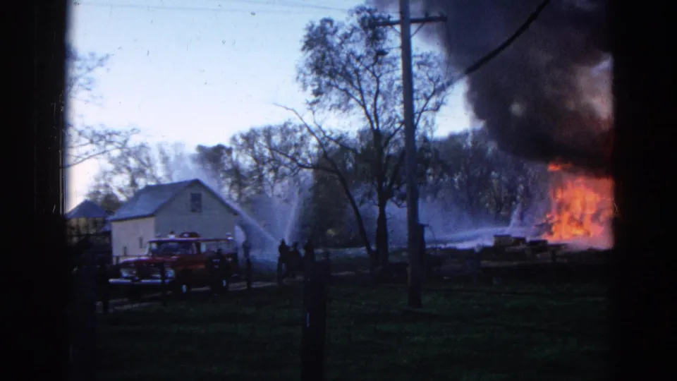 1968 Wauconda, Illinois 8mm frame showing a red fire truck, hose spray, figures, and a house fire with thick smoke.