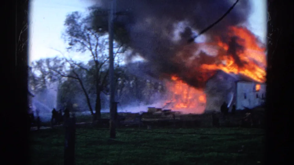 1968 Wauconda, Illinois frame with flames consuming a house, black smoke, hose spray, trees, and small figures nearby.
