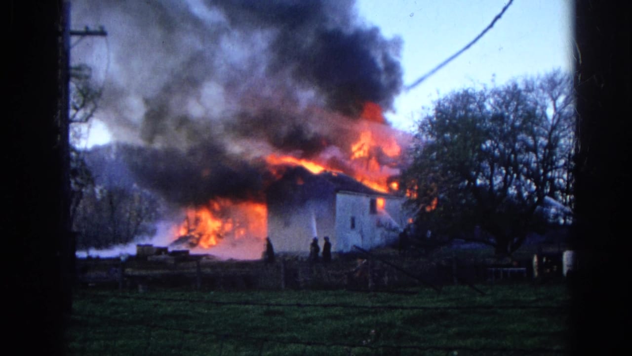 1968 Wauconda, Illinois 8mm frame showing a distant structure engulfed by flames and black smoke across a grassy field.