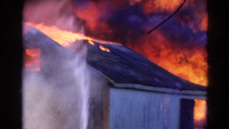 Close 8mm view of a Wauconda structure fire, with bright flames and smoke moving across the roof area.