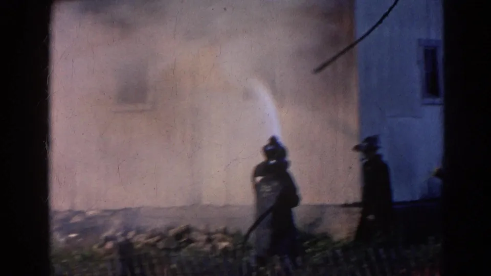 1968 Wauconda, Illinois frame showing firefighters using a hose against a smoky structure fire.