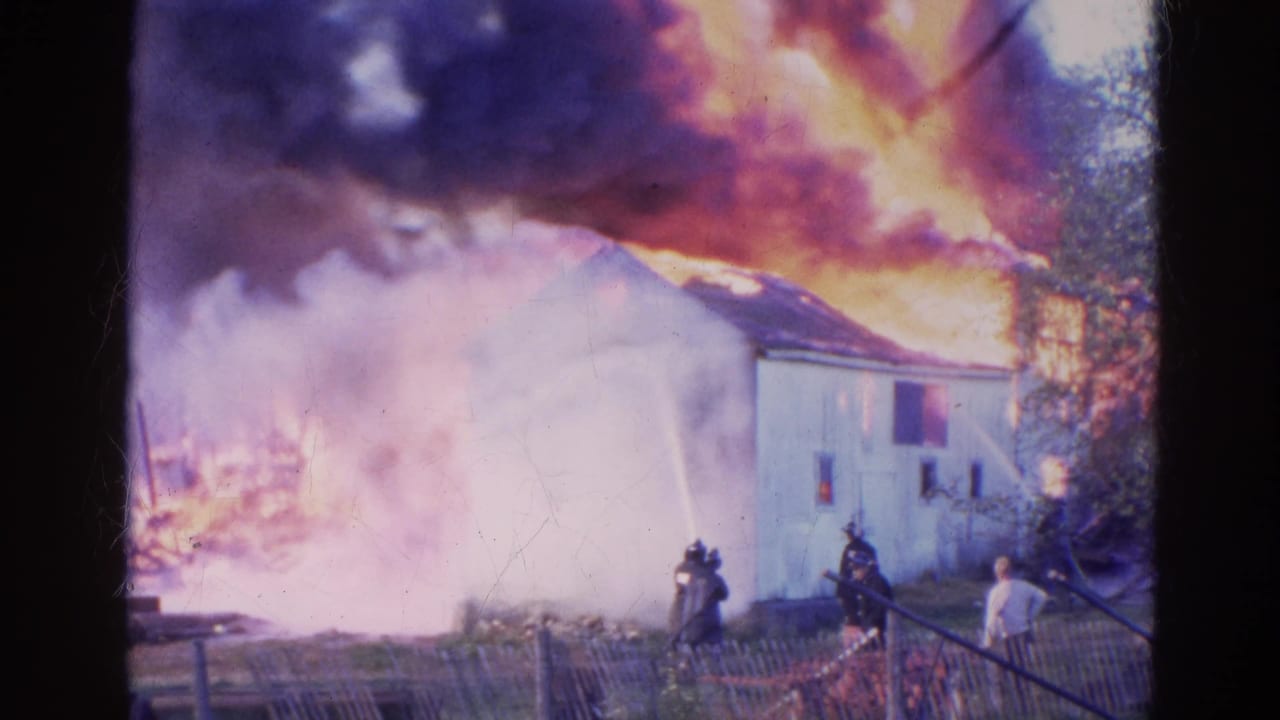 1968 Wauconda, Illinois fire scene with a white building engulfed in flames as firefighters and bystanders stand near a fence.