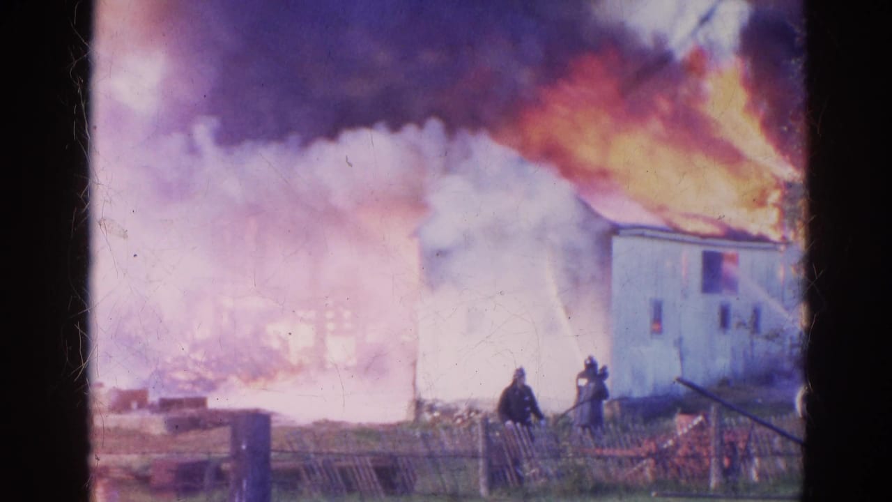 Firefighters in dark gear direct hoses toward a burning white building in this 1968 Wauconda home-movie frame.