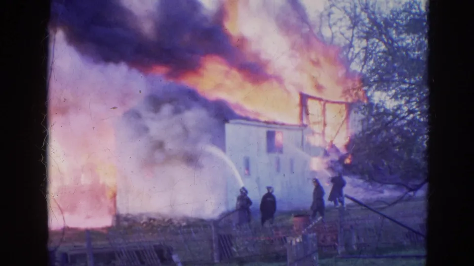 Firefighters in Wauconda, Illinois appear near a hose stream aimed at a white house burning in heavy smoke in 1968 footage.