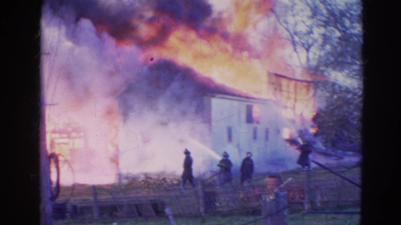 1968 Wauconda home-movie frame of firefighters directing water at a white house engulfed by roof flames and heavy smoke.
