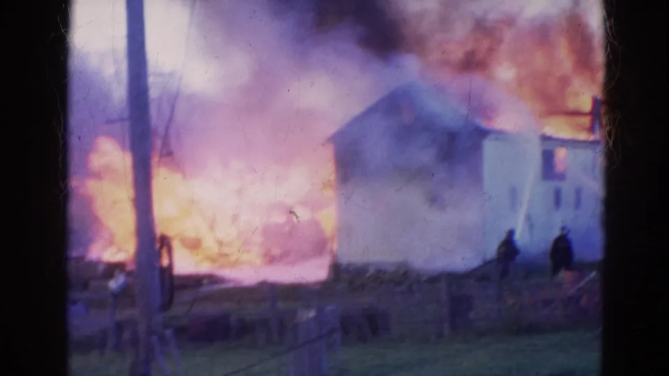 1968 Wauconda fire training footage shows a white structure beside intense flames and smoke, with distant figures at right.