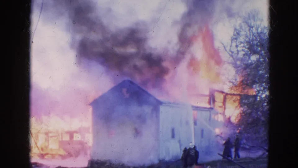 Final 1968 Wauconda frame shows the burning structure amid smoke, flames, bare trees, and distant people near the scene.