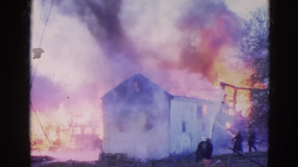1968 Wauconda, Illinois 8mm frame showing firefighters near a small white house surrounded by heavy smoke and orange flames.