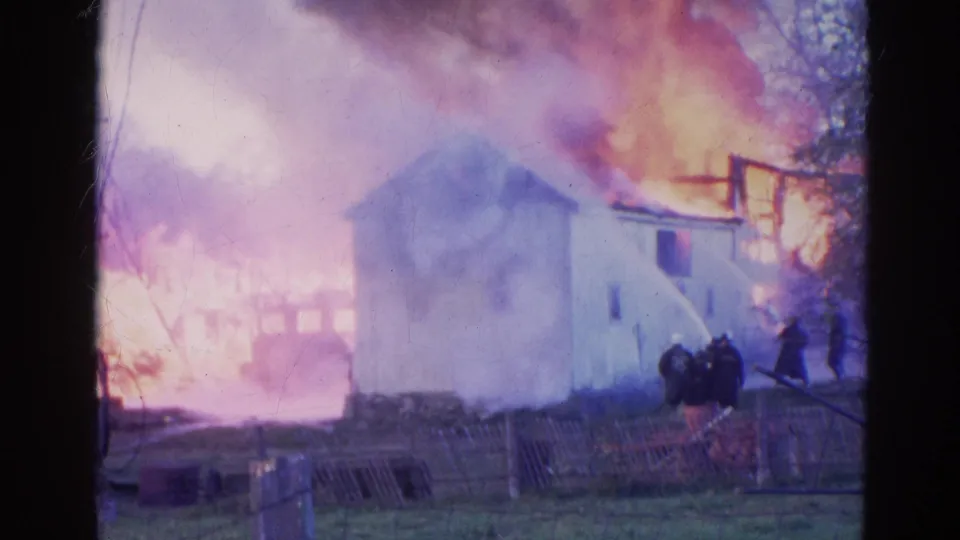 Firefighters in dark coats work with a hose near a smoke-covered house fire in 1968 Wauconda, Illinois home-movie footage.