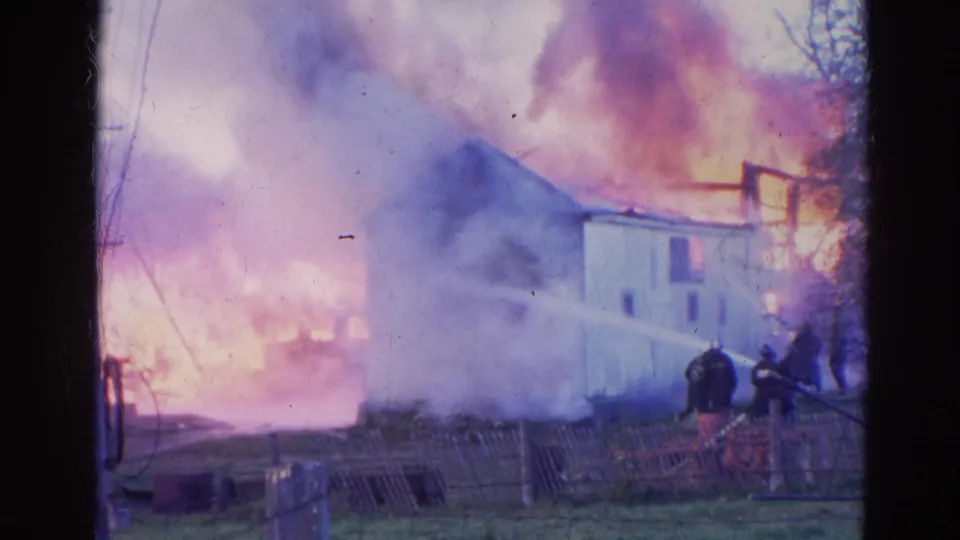 The final 1968 Wauconda, Illinois frame shows firefighters near a fence while flames and smoke rise behind a small white house.