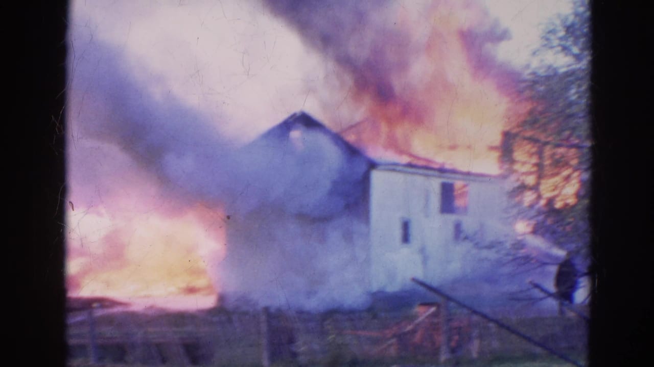 White house burning with heavy smoke and bright flames behind a fence.