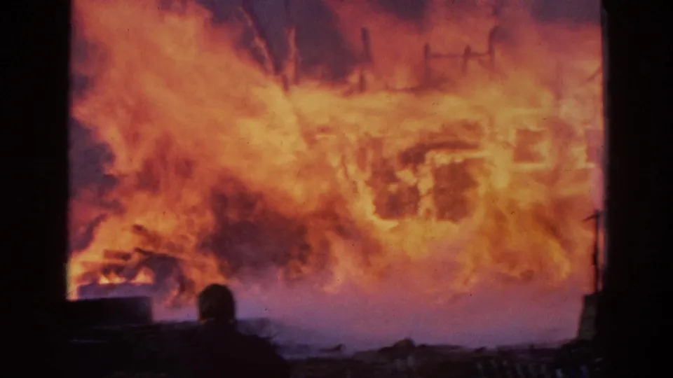 Final frame of the 1968 Wauconda fire clip, with a silhouetted person in the foreground and flames consuming the visible building frame.