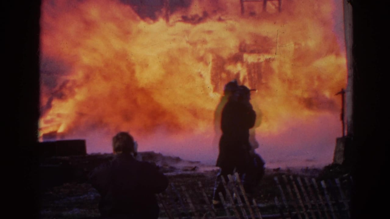 1968 Wauconda, Illinois 8mm frame showing silhouetted figures watching a structure fire from a sheltered vantage point.
