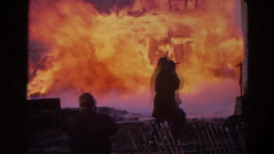 1968 Wauconda, Illinois 8mm frame showing silhouetted figures watching a structure fire from a sheltered vantage point.