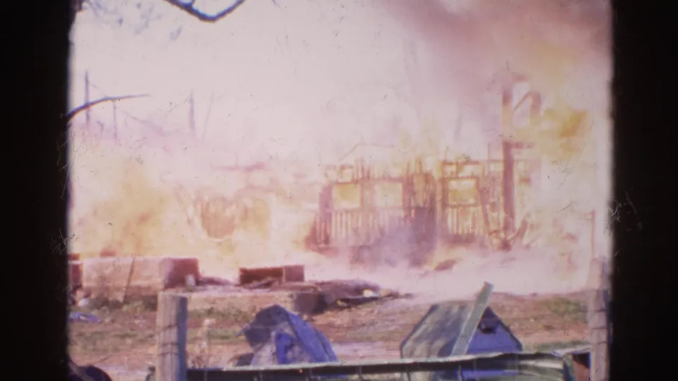 The 1968 Wauconda 8mm clip shows smoke and flames around a damaged wooden structure, with scattered objects in front.