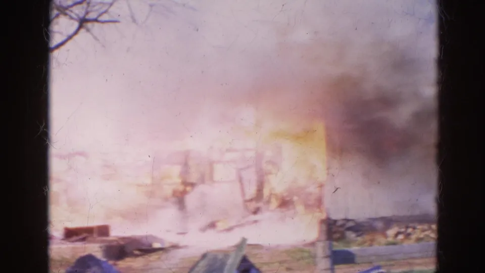 1968 Wauconda 8mm frame with heavy smoke and flames around a burning structure, seen from across a roadside area.