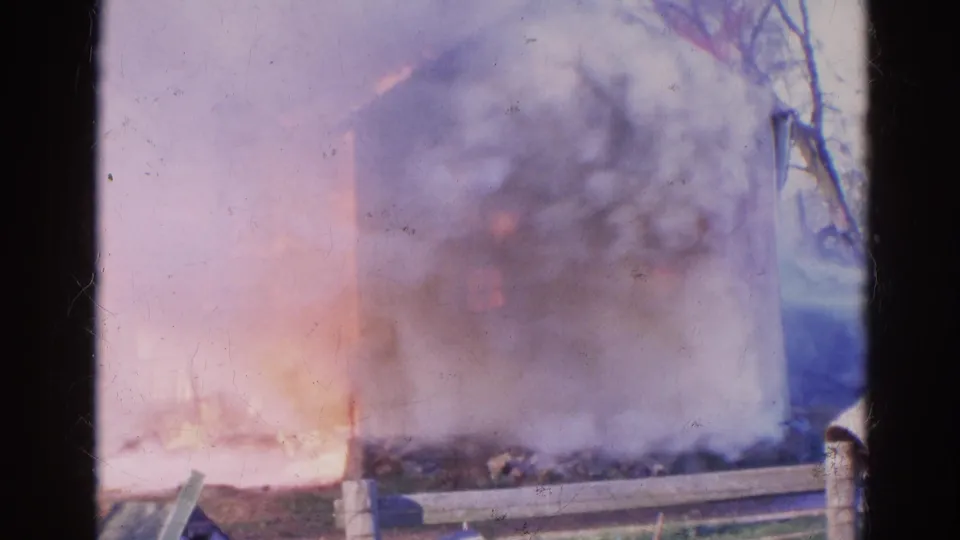 1968 Wauconda 8mm frame showing a large smoke plume, visible flames, roadside posts, and a partially obscured burning structure.