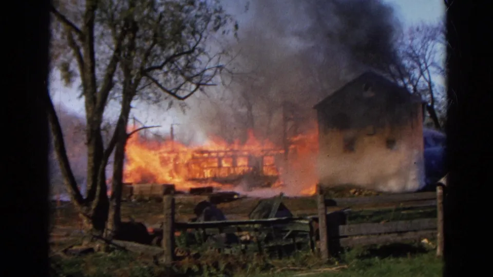 In rural Wauconda, Illinois, flames spread across a wooden structure while smoke rises near trees and a fence.