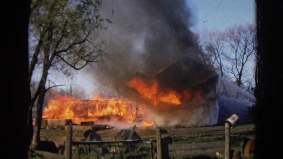1968 Wauconda, Illinois frame showing a rural structure heavily burning with flames spreading low across the scene.
