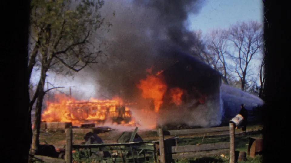 1968 Wauconda, Illinois 8mm frame showing intense flames, thick smoke, and a hose stream striking the burning structure.