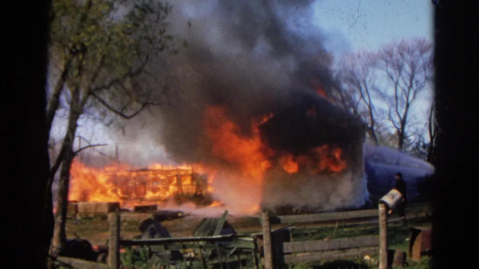 1968 Wauconda, Illinois frame with a firefighter near the right fence line as the burning outbuilding throws flames and smoke upward.