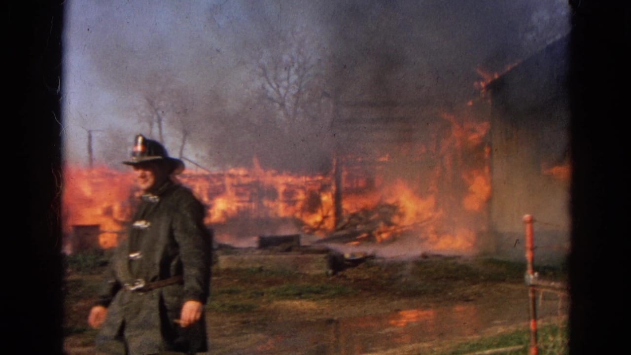 1968 Wauconda, Illinois frame of a firefighter beside hose spray as a burning structure and smoke dominate the background.